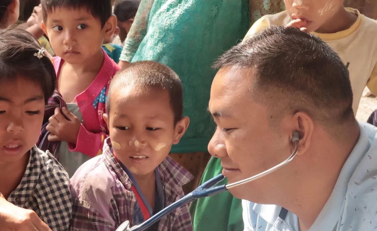 Health and Hope medic using a stethoscope with a child in Myanmar, with other children looking on